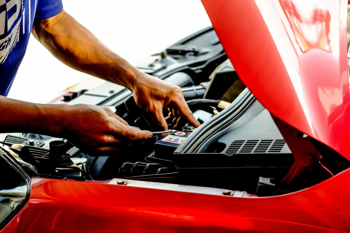 Hands reaching into the engine bay of a red car with the hood up