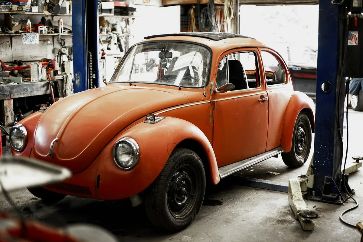 Classic orange Volkswagen Beetle in a repair shop between two lifts