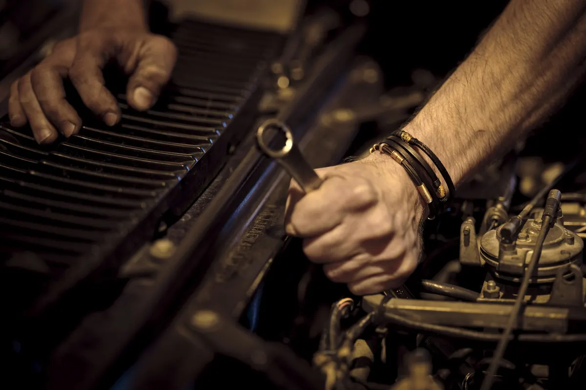 Grease-stained hands turning a wrench on a car engine